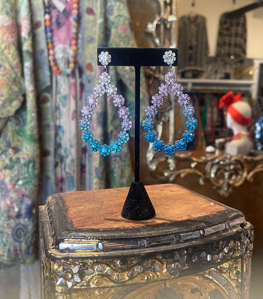 Pair of blue and purple hoop earrings on a black stand with a decorative box in the background.