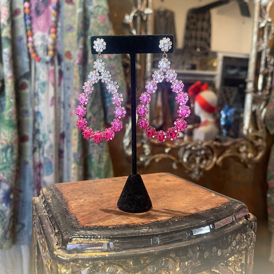 Pink hoop earrings on a black stand with a decorative base.