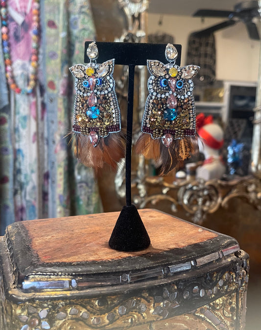 Ornate earrings with feathers and gemstones on a stand in a decorative setting